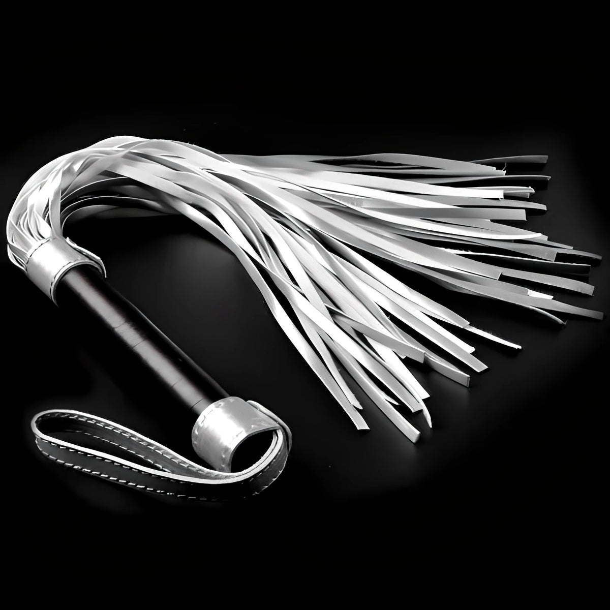 Бич Struggle My Flogger на Lovetoy със сребристи ресни, черна дръжка и ръчна гривна на тъмен фон