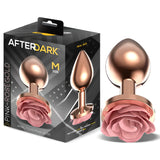 Анален разширител Pink Rose размер M в розово злато с розова роза в основата, до черната кутия на AfterDark