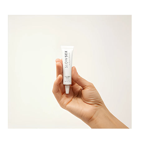 Малка бяла туба Slow Sex Clitoral Balm 10 мл, държана в ръка на светъл фон, за показване на размера на опаковката