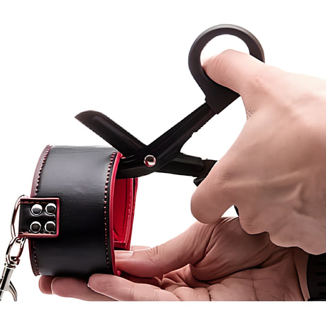 BDSM ножици Ouch! с черни дръжки режат черна кожена маншета с червена подплата, която се държи в ръка