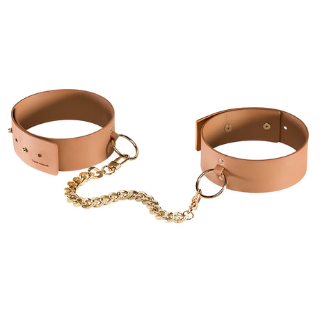 Белезници за крака MAZE на Bijoux Indiscrets: две карамелено кафяви маншета с метални халки, свързани със златиста верижка