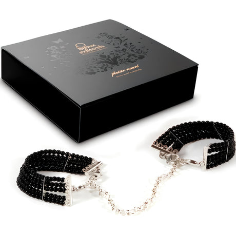 Белезници от черни перли Bijoux Indiscrets със сребристо метално коланче и верижка, до черната луксозна кутия с флорални мотиви