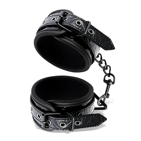 Белезници за крака Black Sapphire на IntoYou: две черни маншета с катарама и капси, свързани с метална верижка с карабинер
