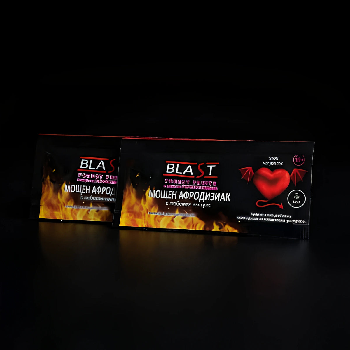 Два черни сашета Blast Forest Fruits с надпис „Мощен афродизиак“, пламъци и червено сърце с крилца на тъмен фон