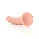 Дилдо Real Rock Slim Realistic 18 cm в телесен цвят, поставено настрани на бял фон, с изглед към кръглата вендуза в основата