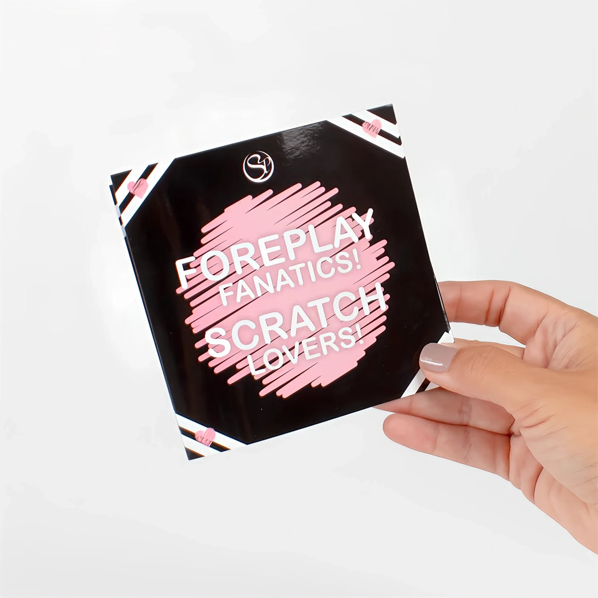 Ръка държи черна квадратна кутия Secret Play Foreplay Fanatics! Scratch Lovers с розов щрих и надпис върху предната част
