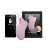 LELO SONA 3 Cruise в розово пред черната си кутия със златен надпис и смартфон с приложението на LELO на екрана