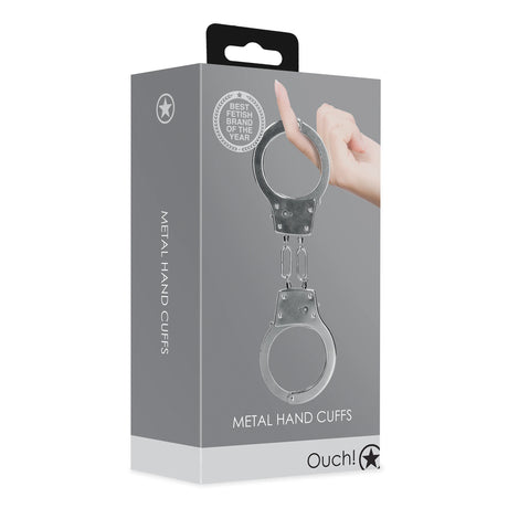 Сива кутия на метални white белезници Ouch! в сребристо с текст Metal Hand Cuffs, значка Best Fetish Brand и ръка на фона