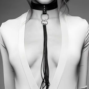 Нашийник с пискюл MAZE на Bijoux Indiscrets с метални халки и дълъг пискюл от тънки ленти, носен върху бяла блуза с дълбоко деколте