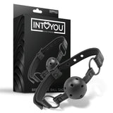 Черен наустник Black Shadow на IntoYou с перфорирана топка и каишка с метални халки, показан пред черната си кутия с лого