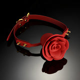 Наустник Rose Ball Gag на Zalo в червено със златисти метални капси и катарама, поставен върху тъмна лъскава повърхност