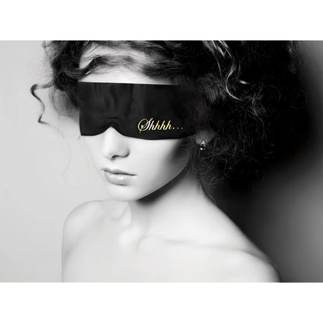 Жена с къдрава коса носи черната сатенена лента за очи Shhh Blindfold с златен надпис „Shhhh…“, черно-бяла снимка