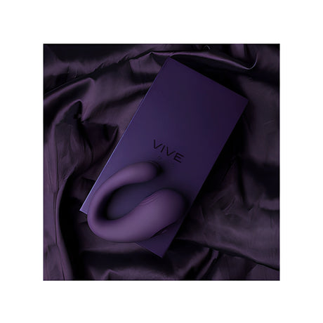 Лилав стимулатор Yoko на Vive, поставен върху лилавата кутия с надпис VIVE, върху сатенен плат в същия тъмен цвят