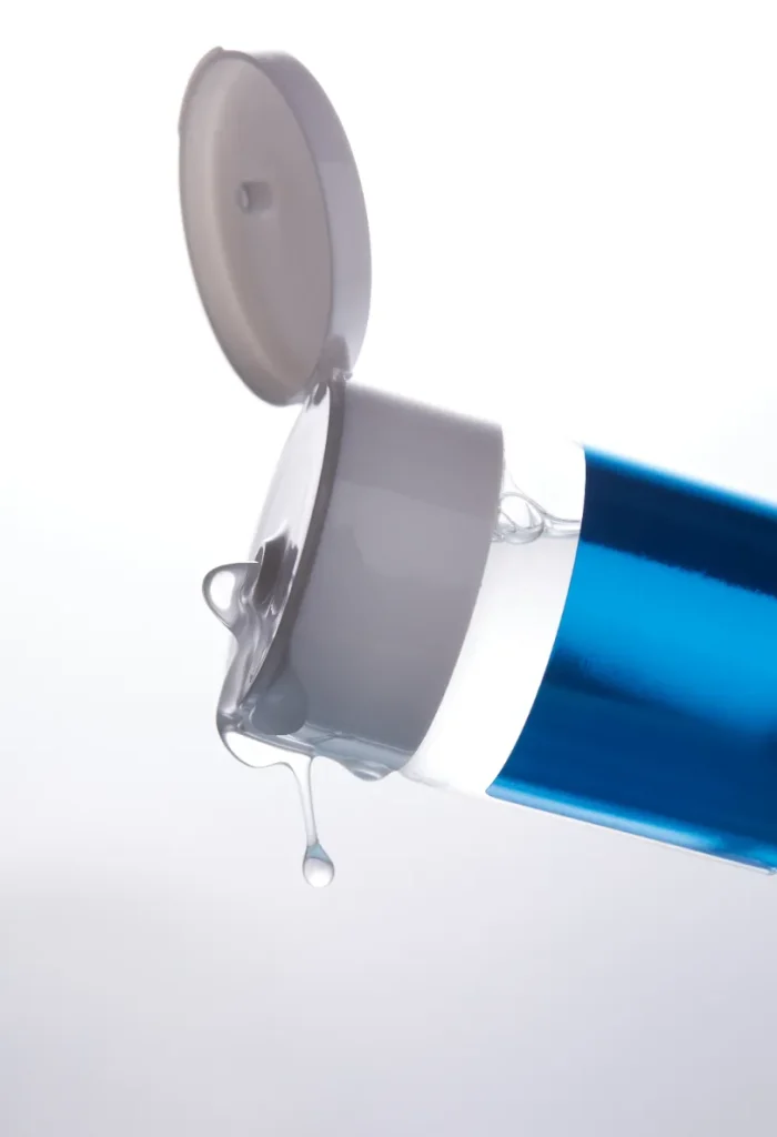 Близък кадър на лубрикант с прозрачна гелообразна текстура, капещ от отворена туба.