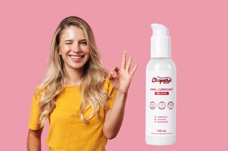 Усмихната млада жена с жълта тениска и жест „ОК“ до бутилка анален лубрикант Cleopatra Relaxing – 150 мл, на водна основа, безопасен за латекс.